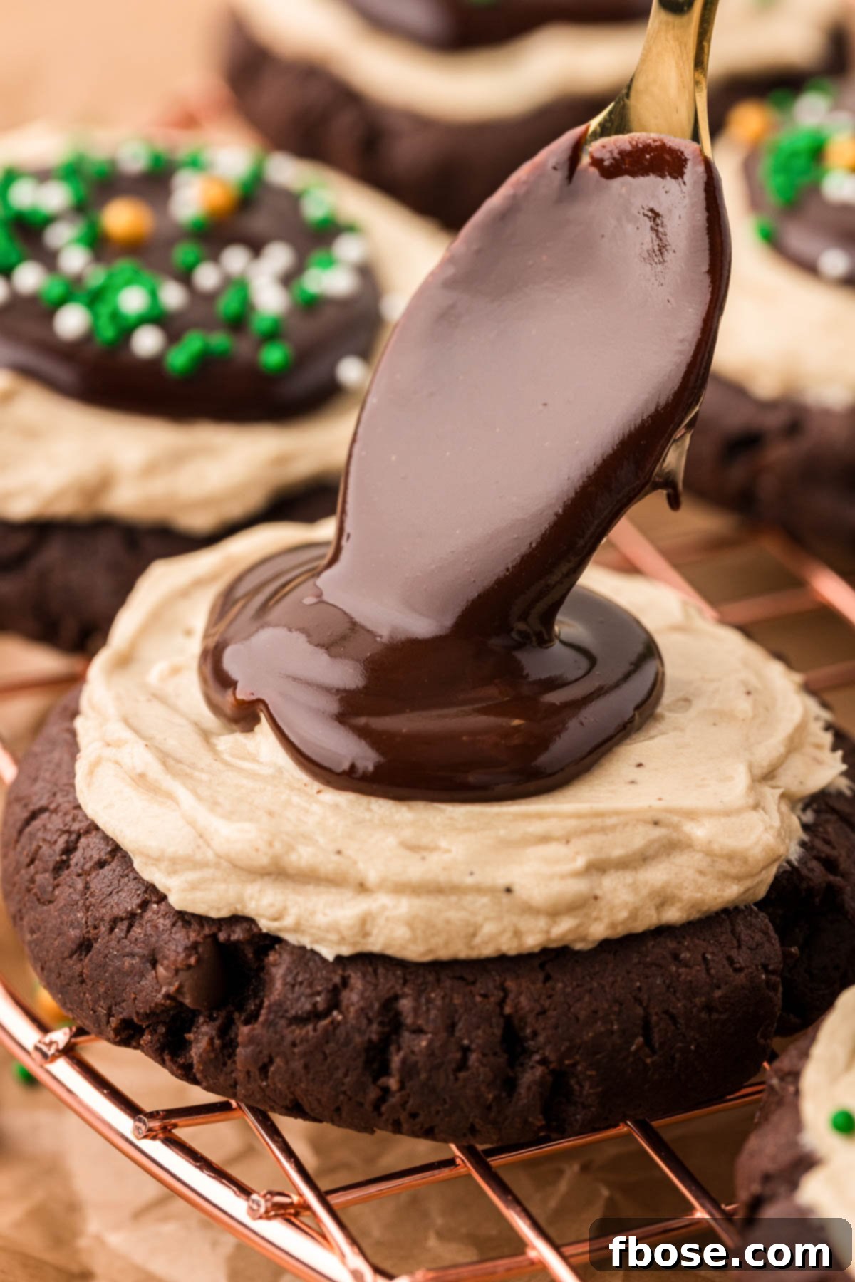 Chocolate ganache being spooned onto a frosted cookie.