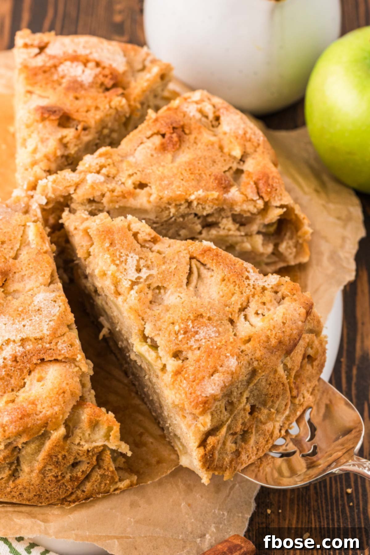 A delicious slice of Irish Apple Cake being carefully pulled away from the whole cake, showing its moist interior and apple chunks.