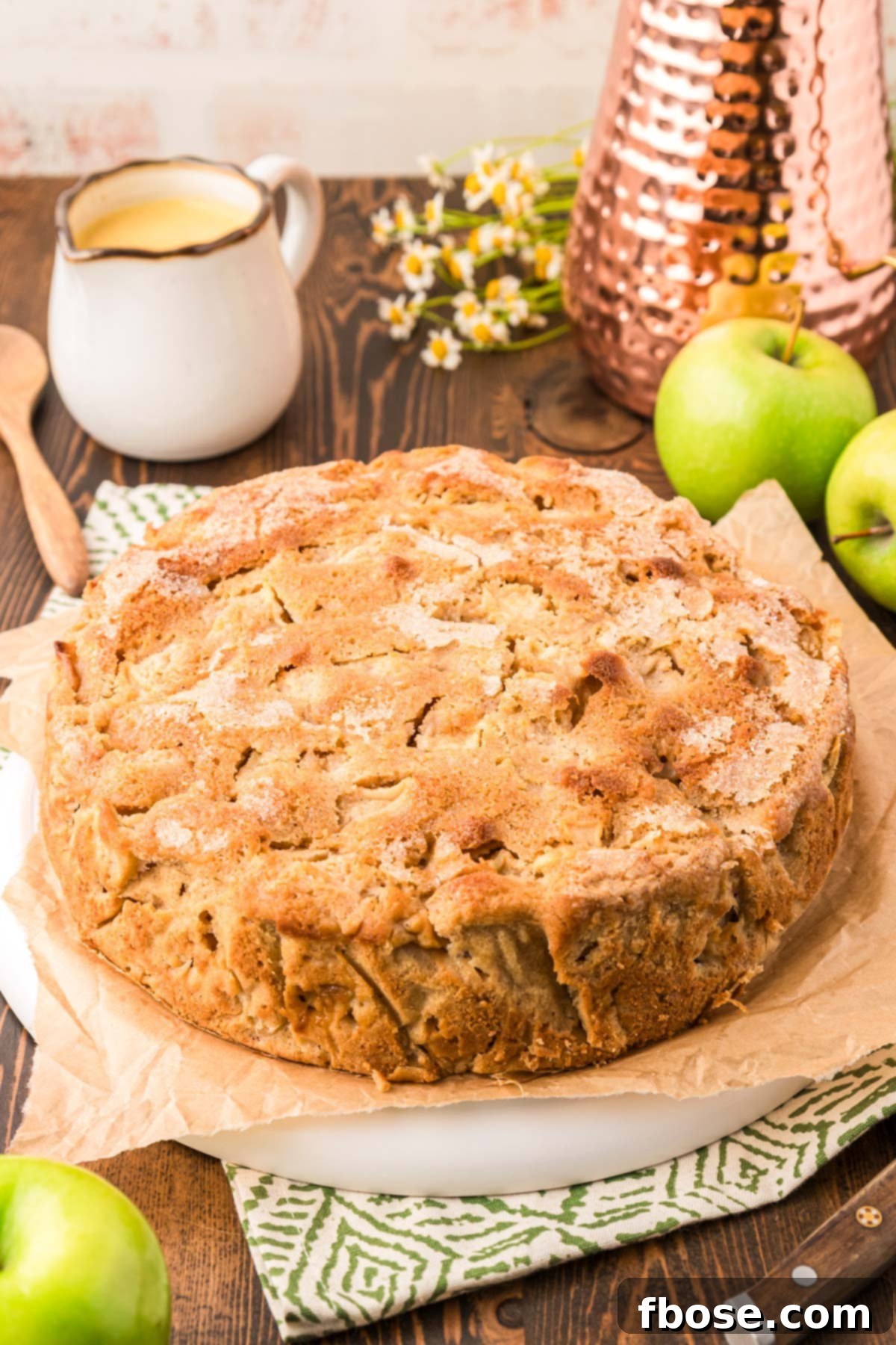 A stunning photograph of a whole round Irish Apple Cake, golden brown and perfectly baked, presented on a pristine white plate.