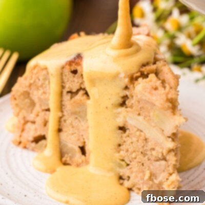 Vanilla custard being poured on Irish Apple Cake slice on a white plate.