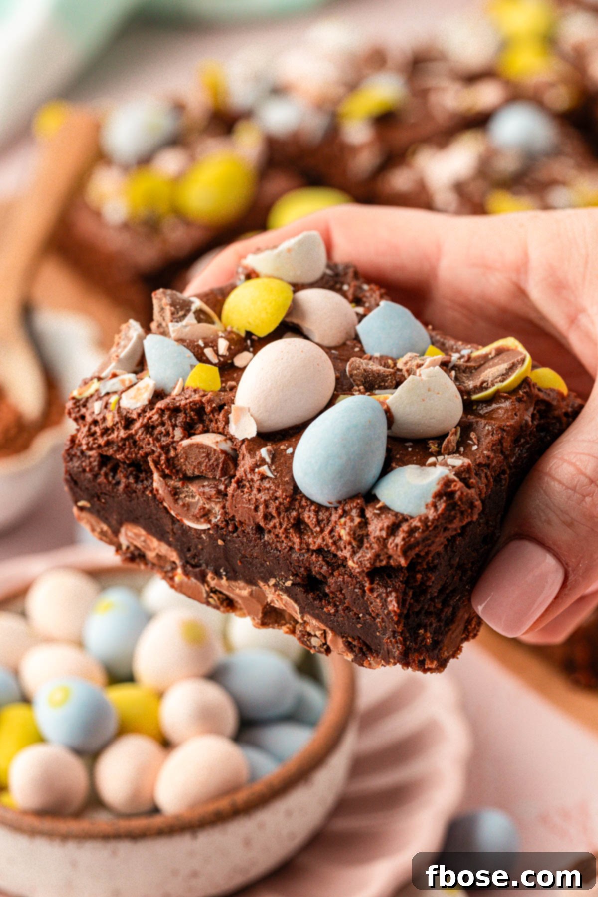Molten Cadbury Egg Brownies 7 A woman's hand gently holds a single Cadbury Mini Egg Brownie up to the camera, ready for a bite.