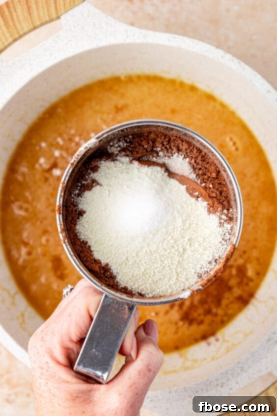 A sifter sifting flour and cocoa into butter and sugar in a pot to make brownie batter.