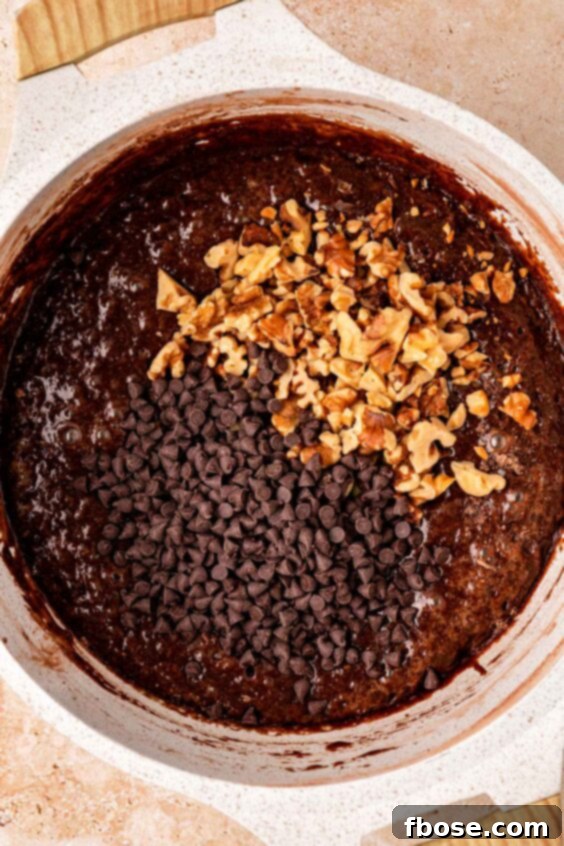 Chocolate chips and walnuts being mixed into a pot of brownie batter.