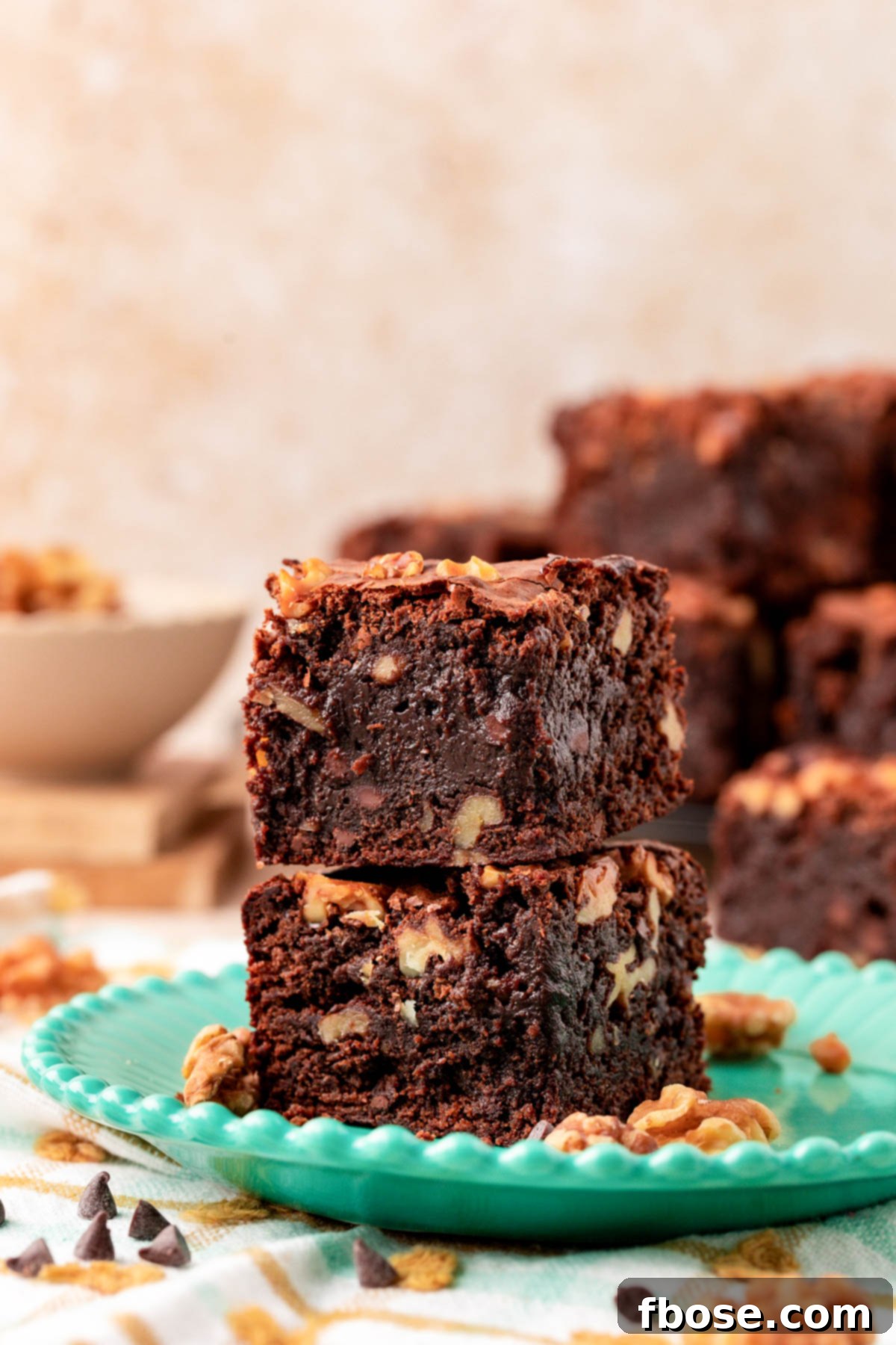 Two walnut fudge brownies stacked on a teal plate.