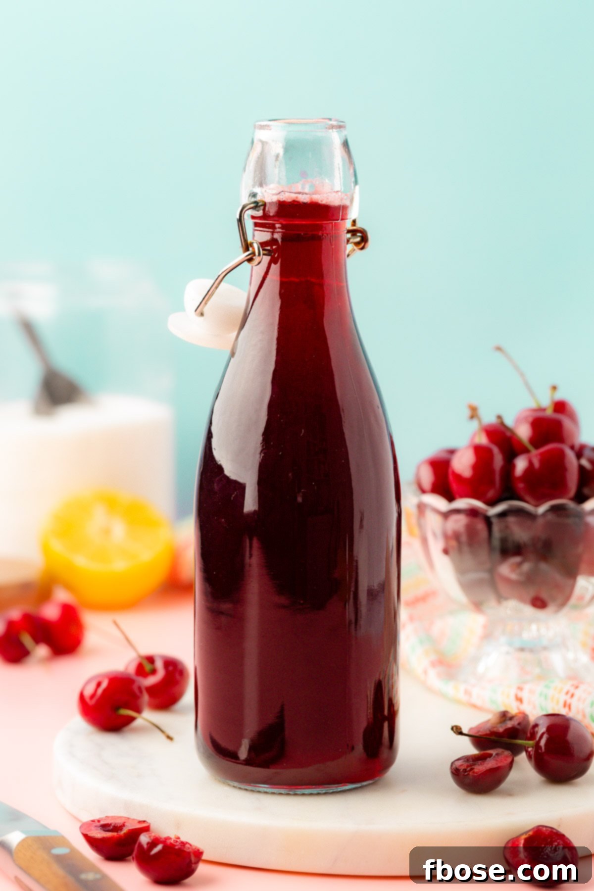 A bottle of homemade cherry simple syrup, gleaming with rich color, stands on a rustic wooden table, suggesting its natural and refreshing qualities.