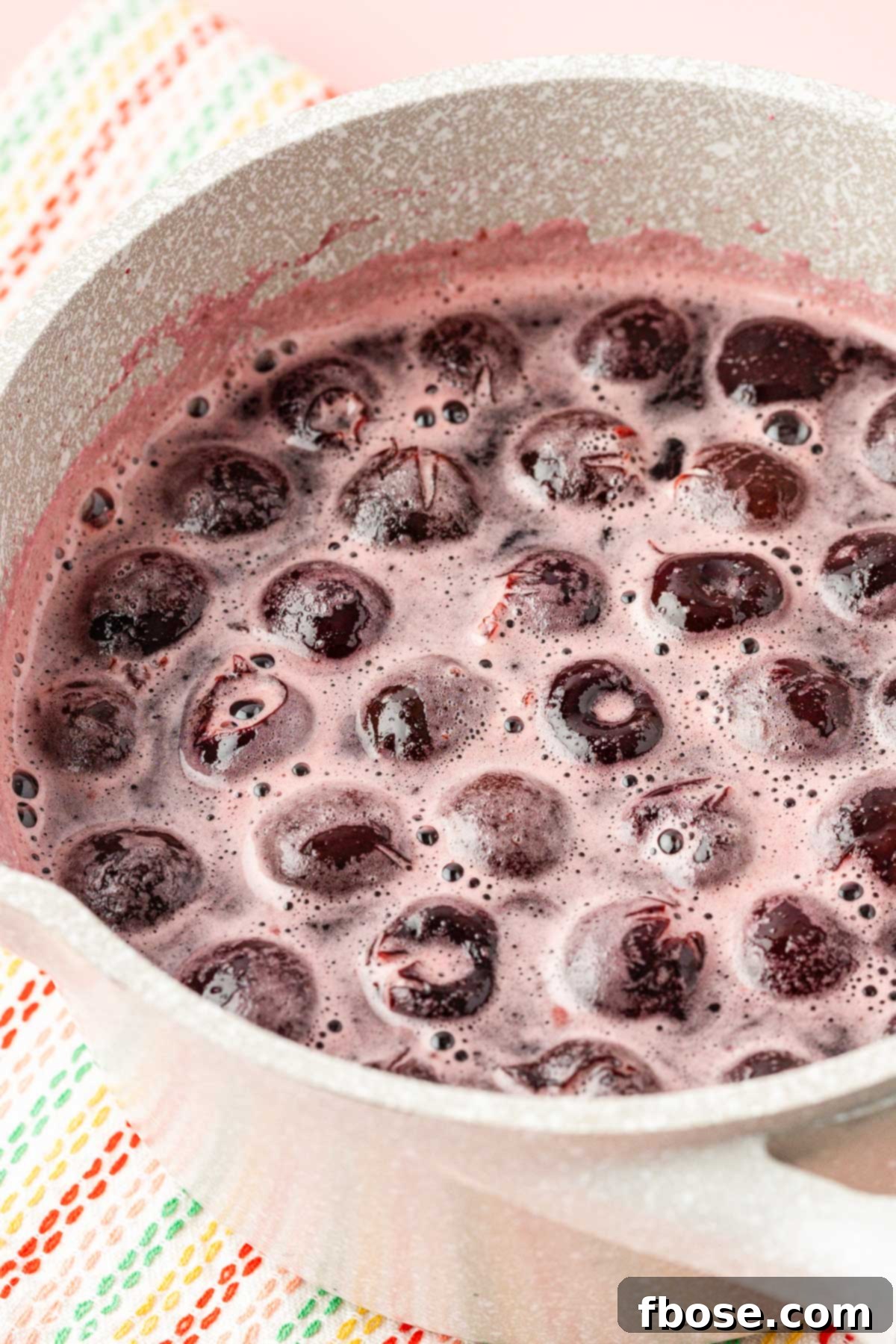 Close-up of dark pitted cherries simmering gently in a pot with sugar and water, creating the flavorful base for the simple syrup.