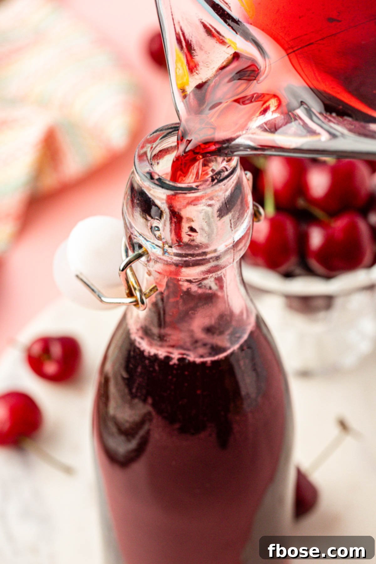 Homemade cherry simple syrup being carefully poured into a clear glass bottle using a funnel, ready for storage.