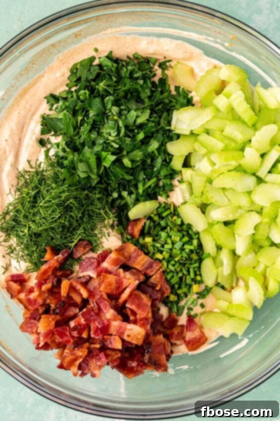 herbs, bacon, and celery in a bowl with dressing for potato salad.