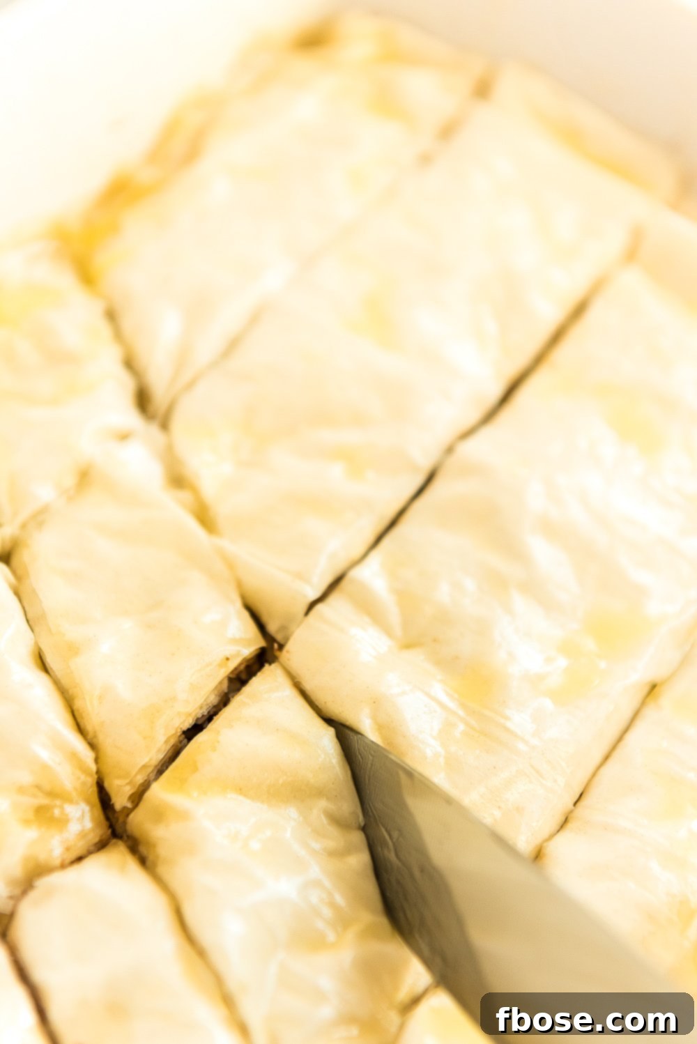Effortless Homemade Baklava 8 Baklava being cut with a large knife before going in the oven.