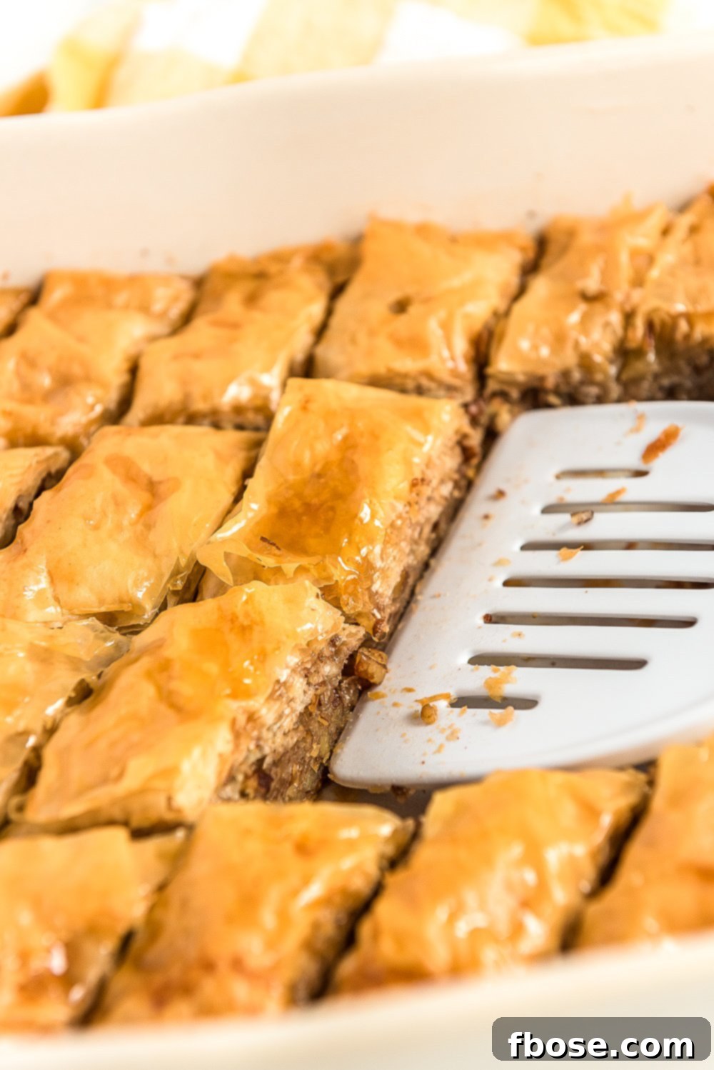 Effortless Homemade Baklava 10 Spatula scooping pieces of baklava out of a baking dish.