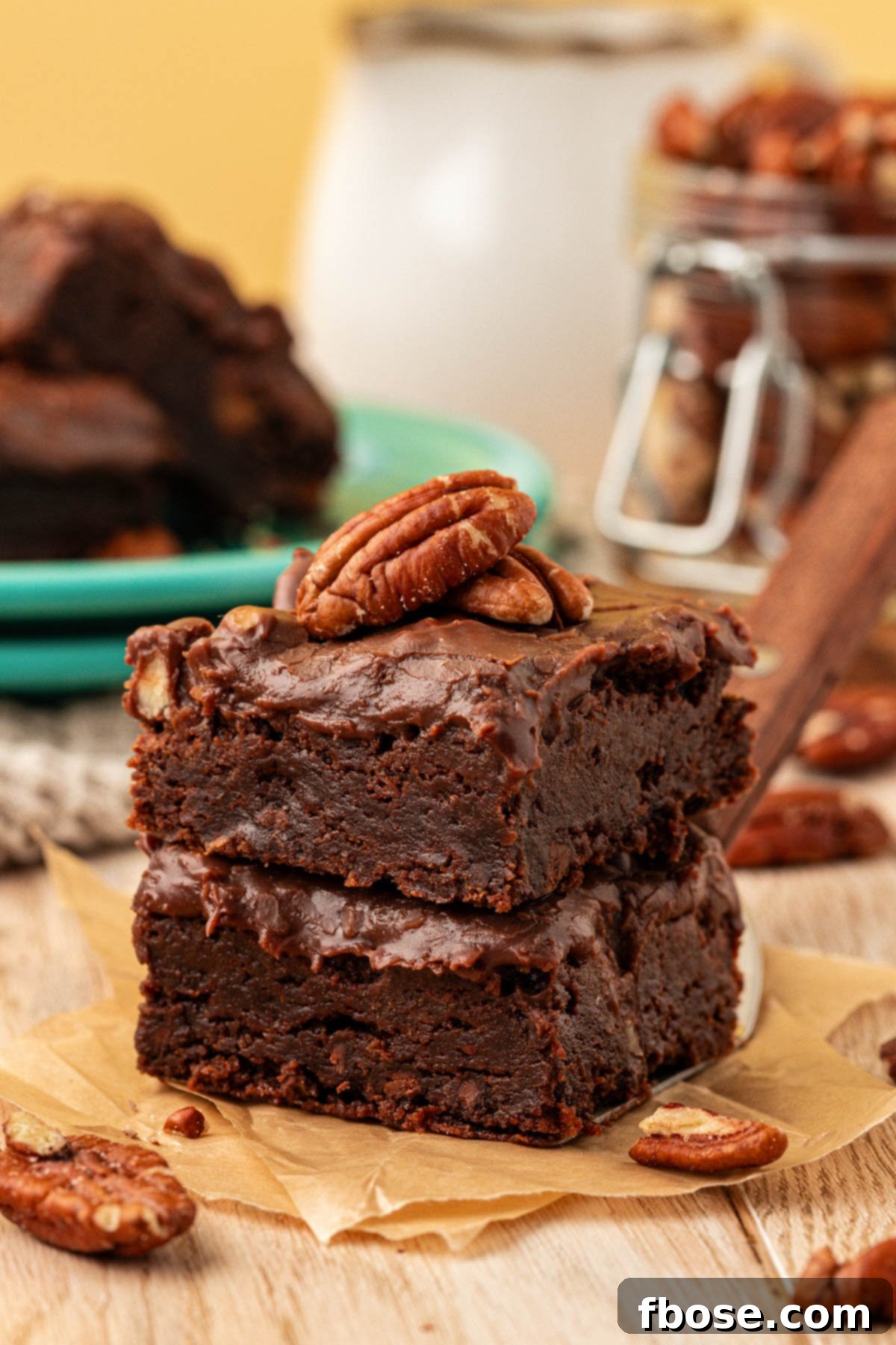 Two Texas Sheet Cake Brownies stacked on a piece of parchment on a table, showcasing their thick icing and pecan topping.