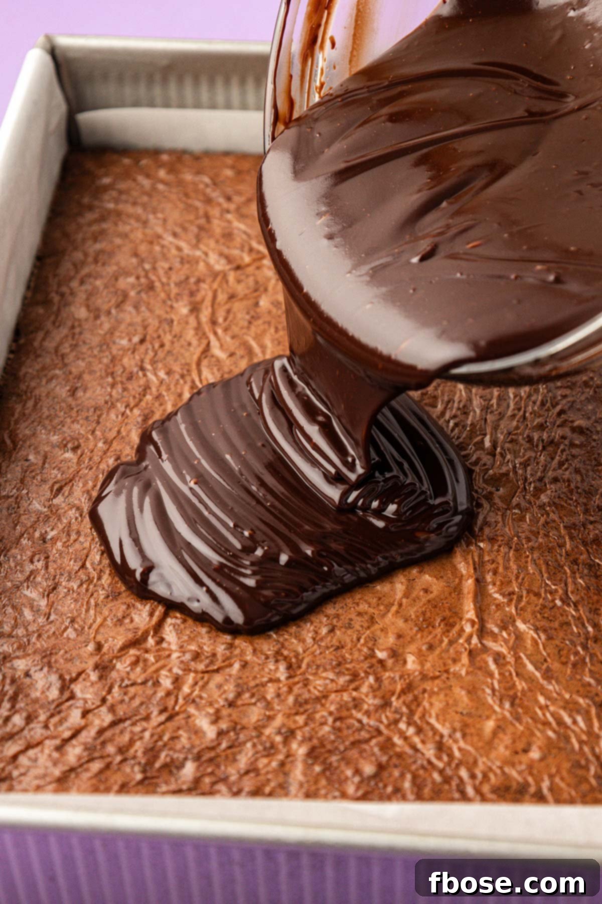 Ganache being poured over the top of baked brownies, ready for sprinkles.