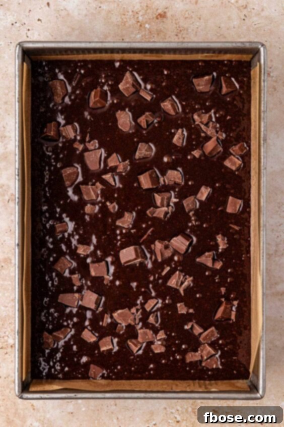 Chocolate chunk brownie batter in a 9x13-inch pan ot a table.