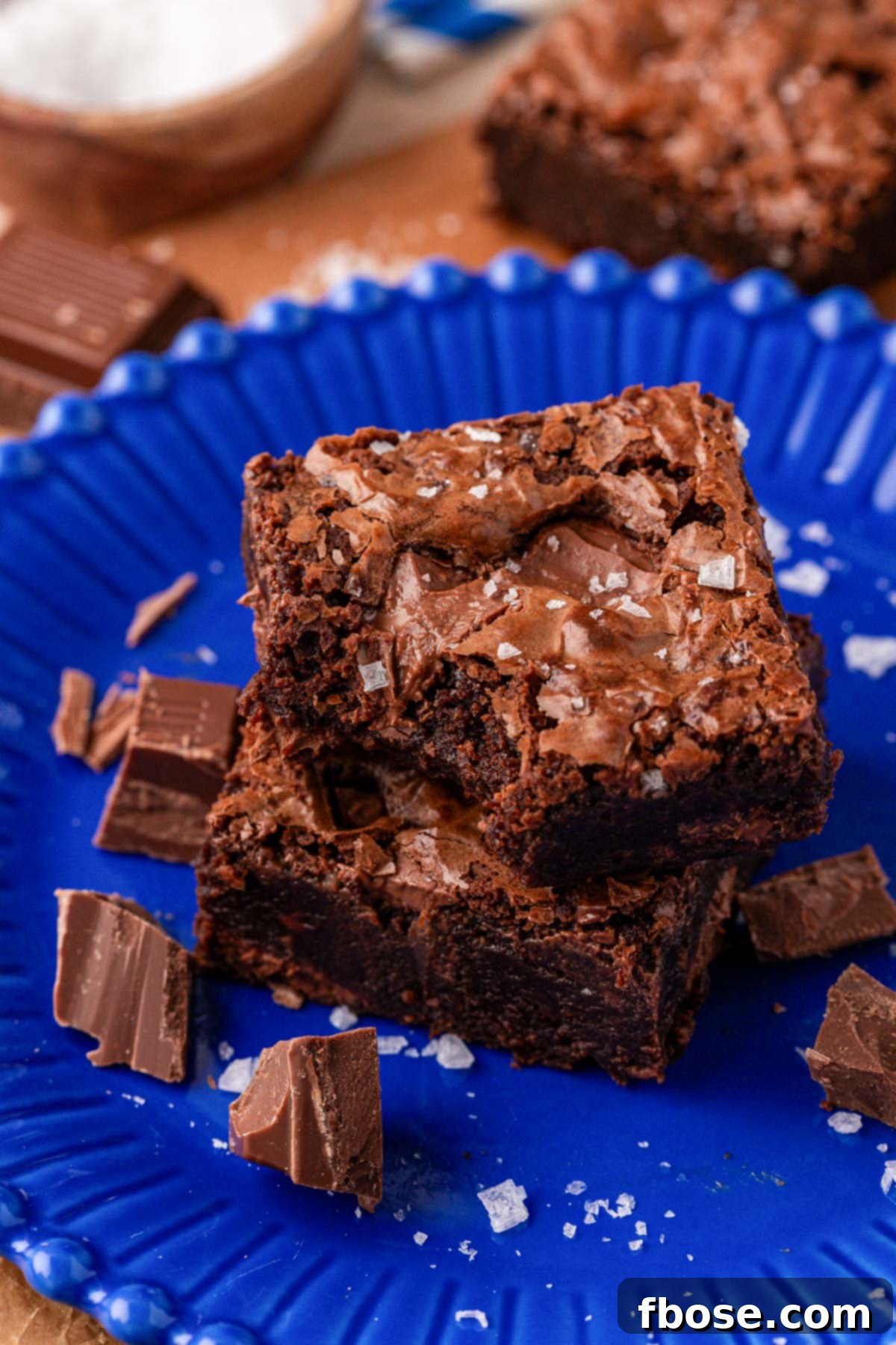 Two chocolate fudge brownies on a blue plate, one is missing a bite.