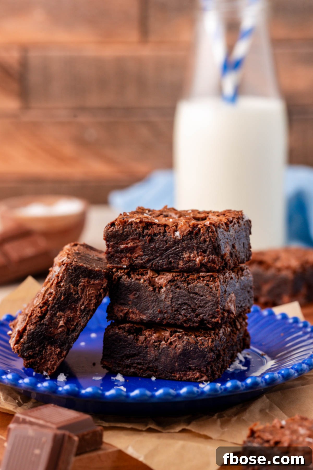A stack of three brownies on a blue plate with another brownie leaning against them.