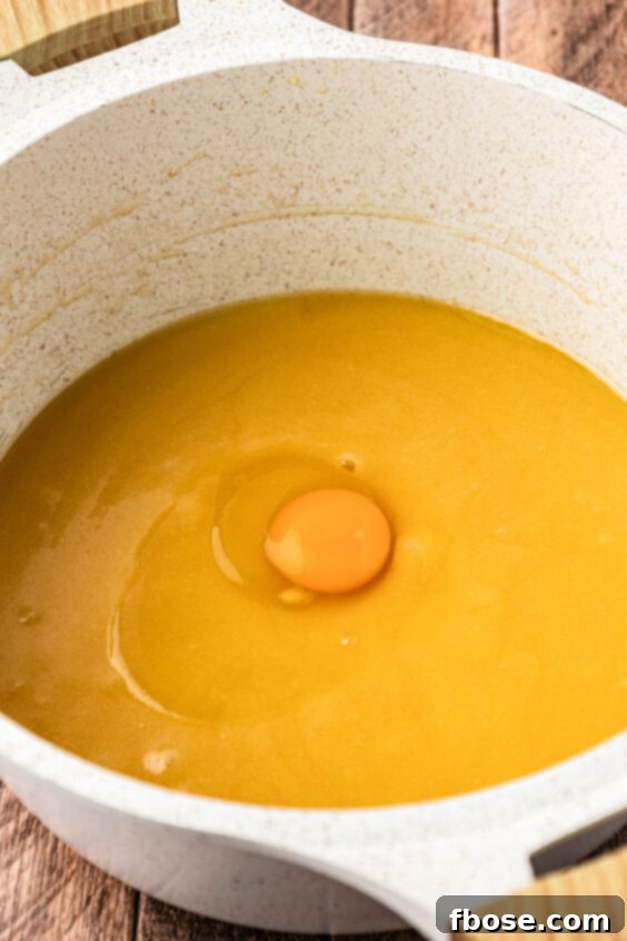 Egg being added to a pot with other ingredients to make brownie batter.