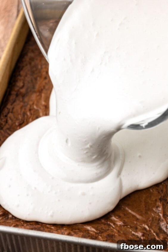 Marshmallow cream being poured over the top of the brownies.