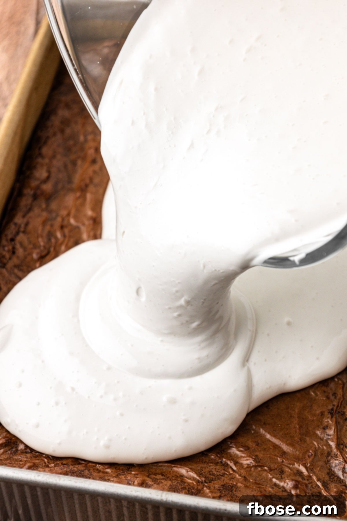 Marshmallow cream being poured over the top of the brownies.