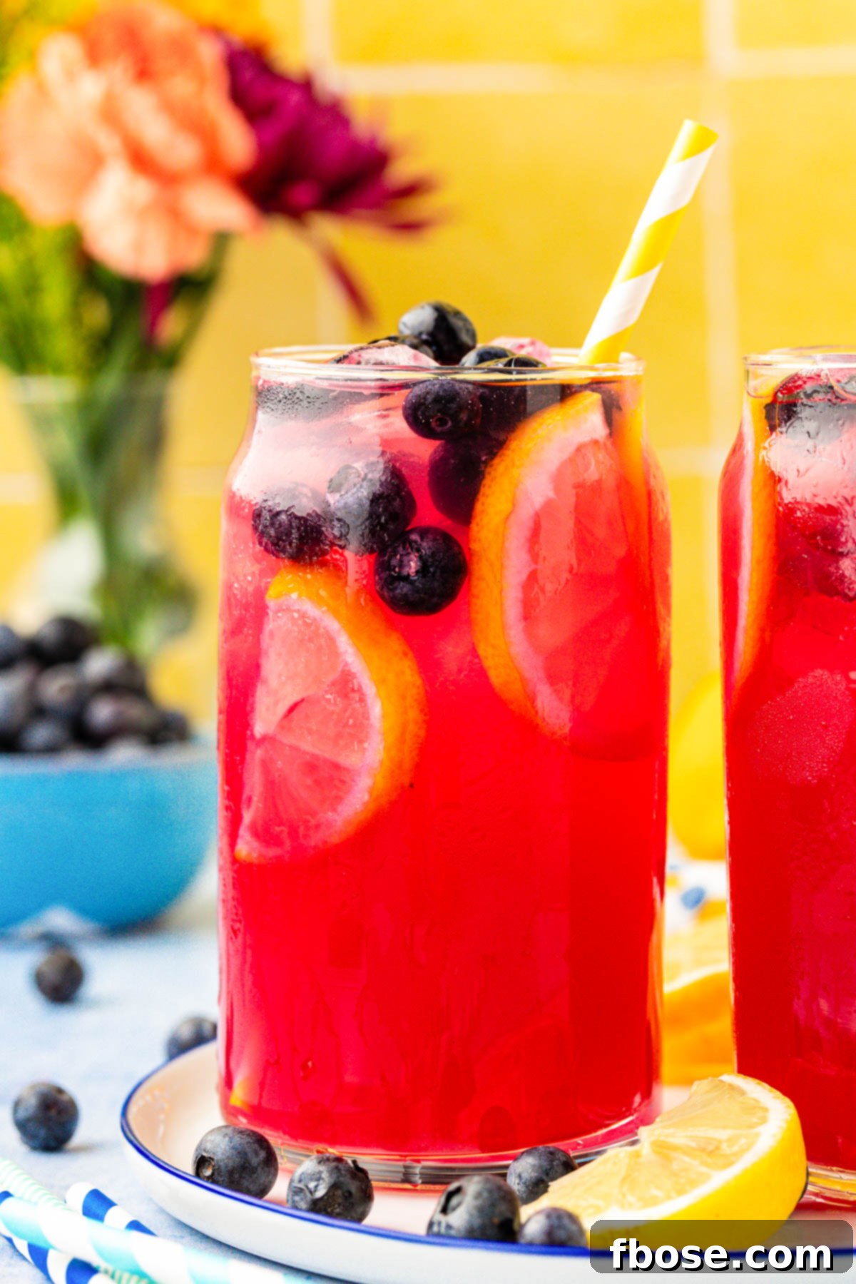 Glasses of homemade blueberry lemonade on a sunlit table, garnished with fresh blueberries and lemon slices.