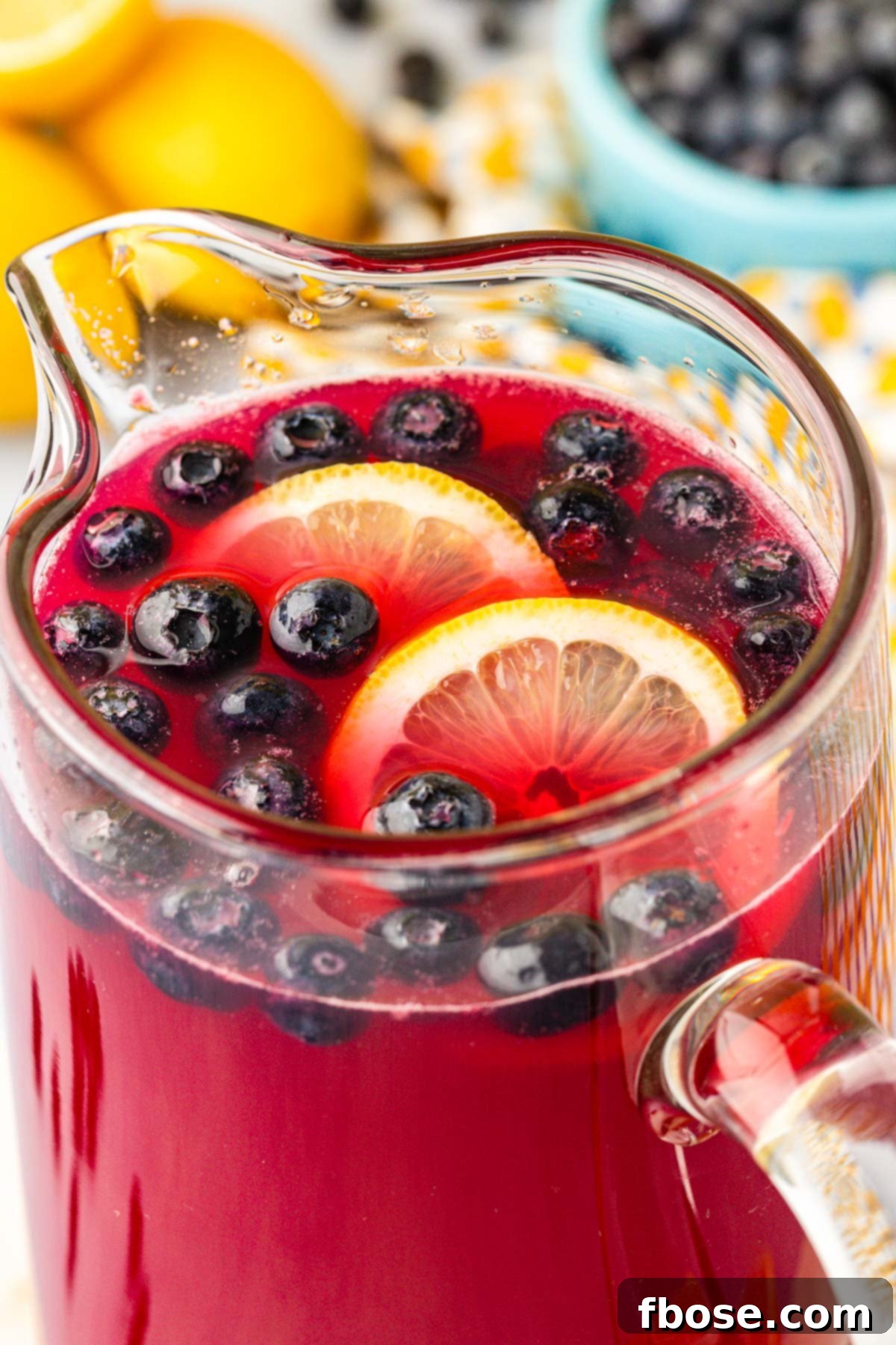A large glass pitcher filled with homemade blueberry lemonade, garnished with fresh lemon slices and blueberries, ready to be served.