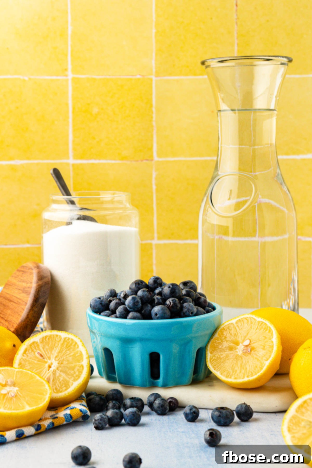 Fresh ingredients laid out on a wooden table: ripe blueberries, yellow lemons, and a bowl of sugar, all essential for making blueberry lemonade.