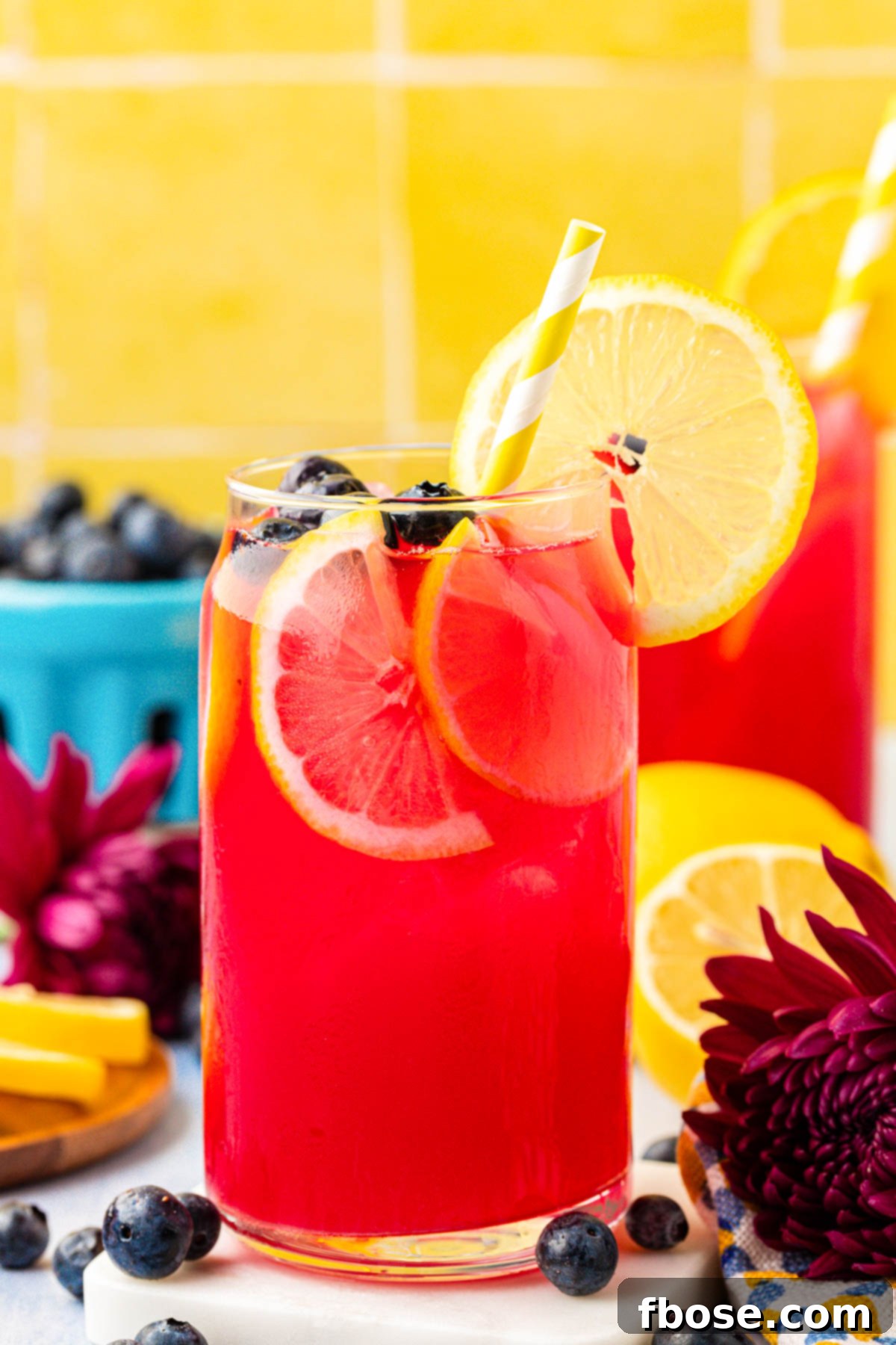 A glass of blueberry lemonade with a straw, garnished with lemon and blueberries, capturing the essence of a refreshing summer drink.