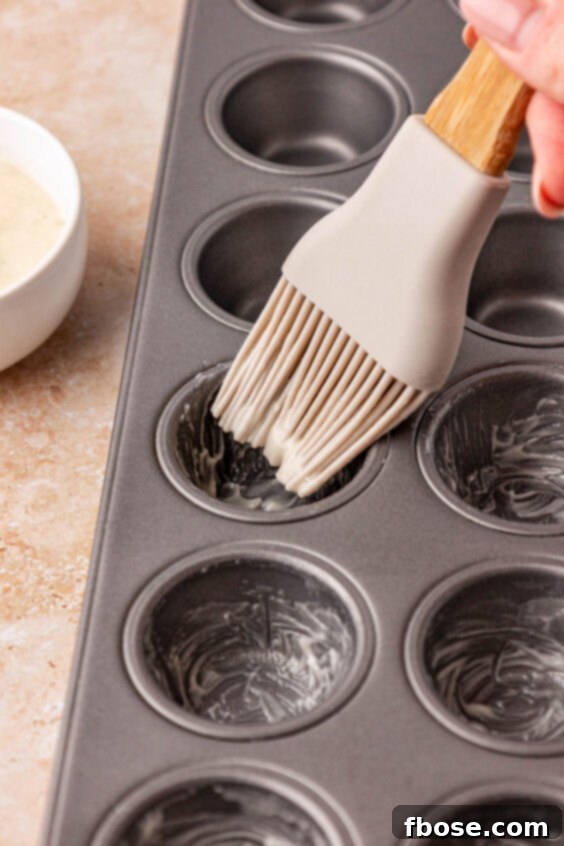A silicone pastry brush coating the inside of mini muffin tin wells with nonstick paste.