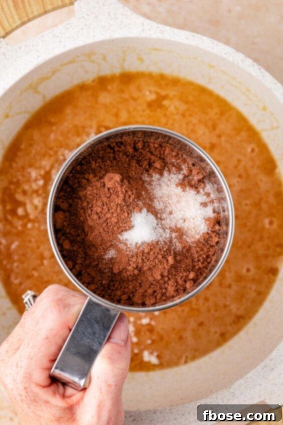Dry ingredients being sifted into a pot with a butter and sugar mixture.