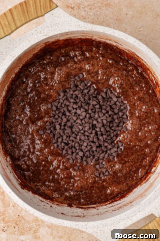 Mini chocolate chips being added to a pot with brownie batter in it.
