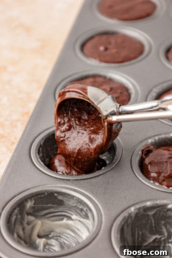 Brownie batter being added to a mini cupcake pan with a cookie scoop.