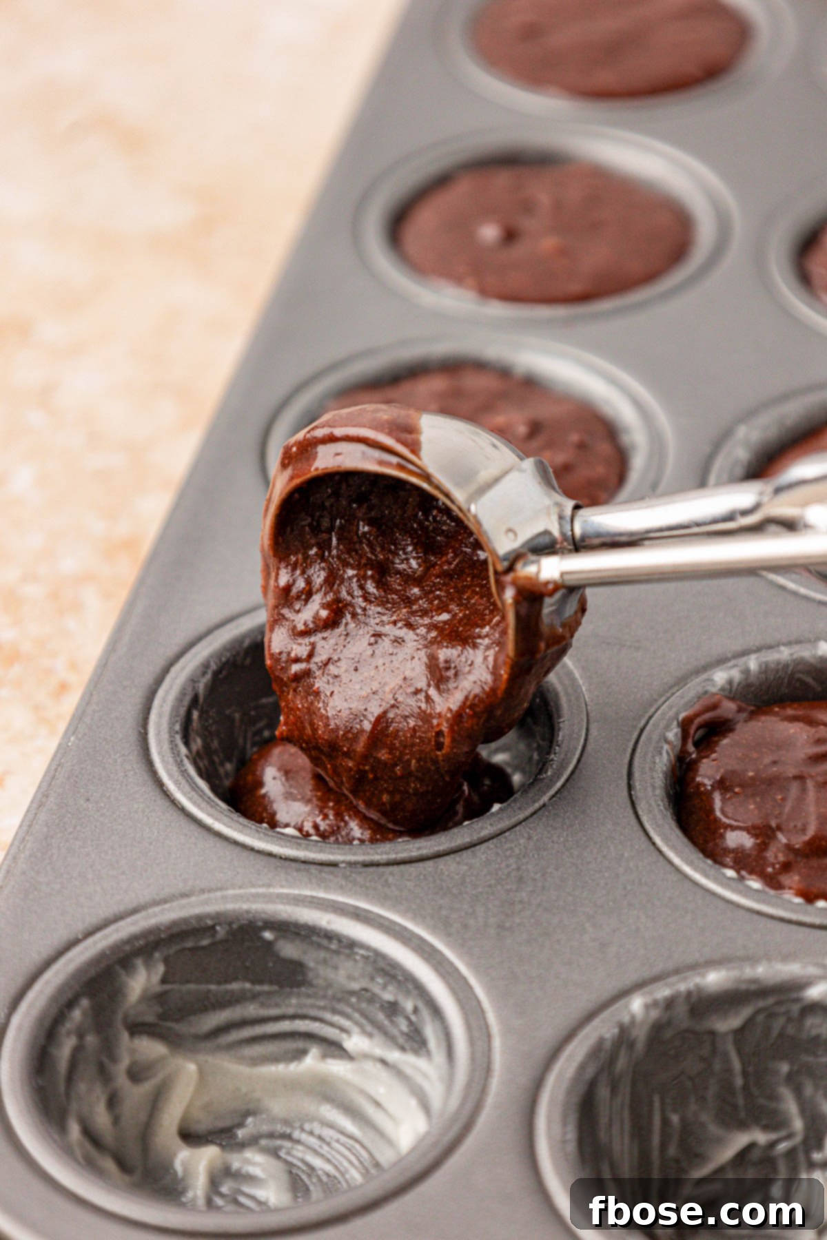 Brownie batter being added to a mini cupcake pan with a cookie scoop.