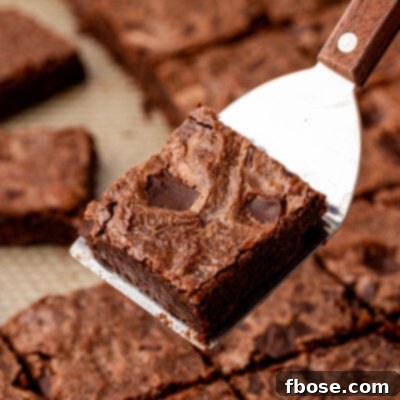 A spatula holding a sheetpan brownie above a pan of brownies.