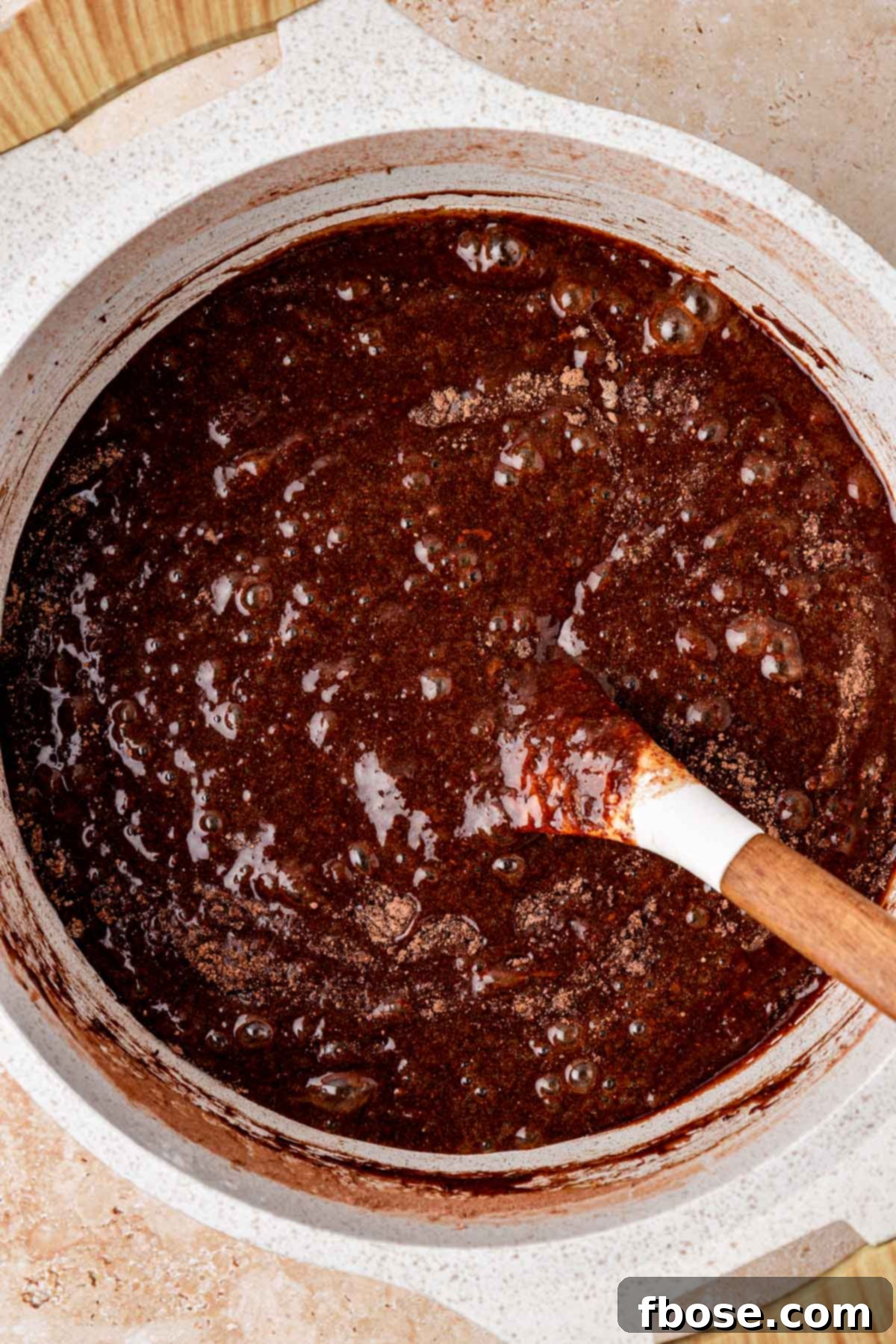 Chocolate chunks being stirred into brownie batter in a pot.