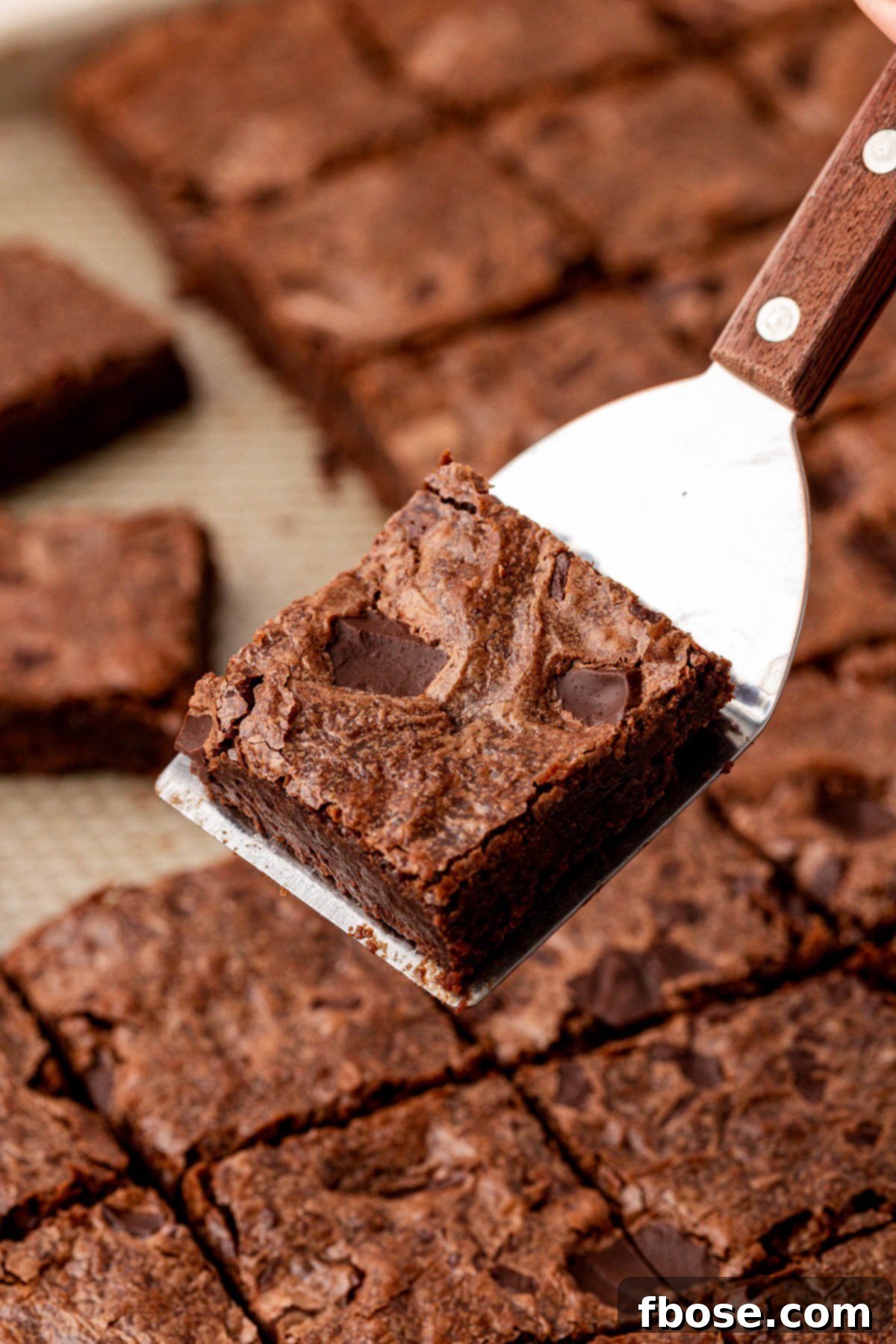 A spatula holding a sheetpan brownie above a pan of brownies.