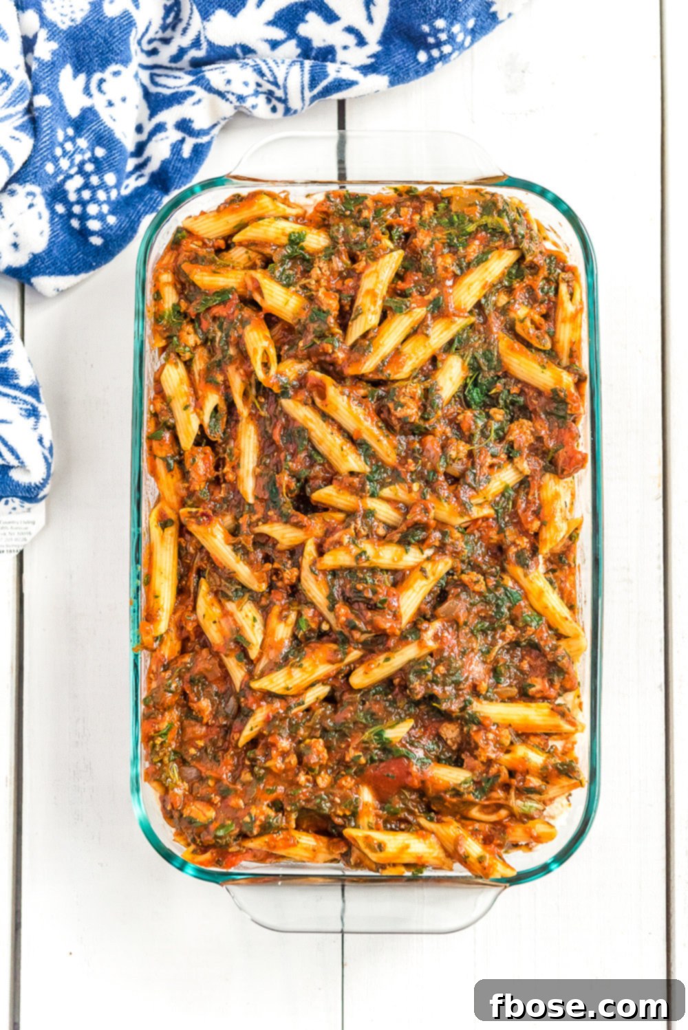 A large casserole dish filled with baked Turkey Florentine pasta, resting on a white table with a blue napkin.