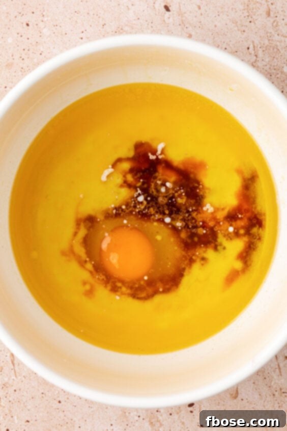 Egg being added to a bowl with melted butter and oil.