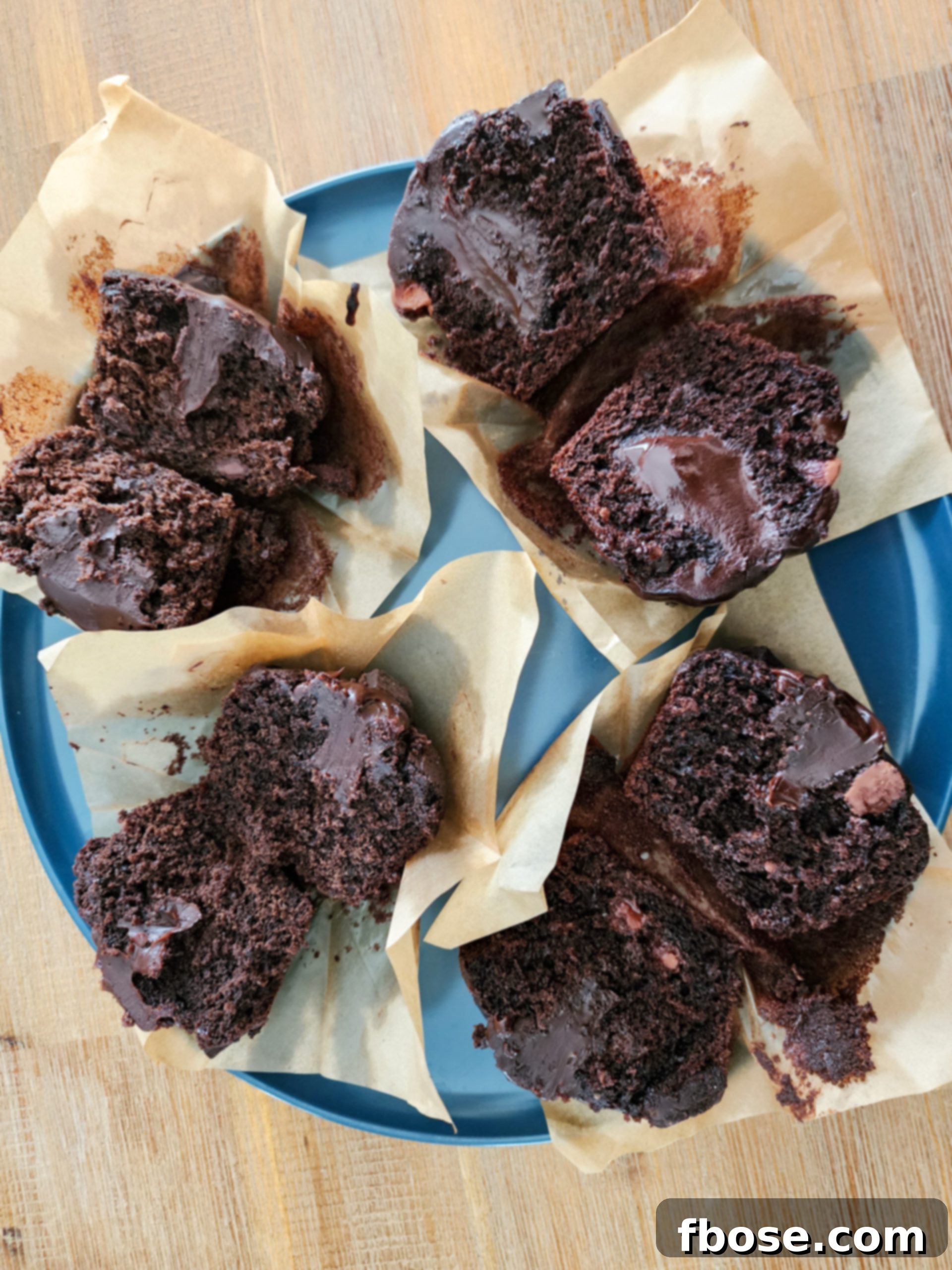 Four chocolate muffins cut in half on a blue plate, displaying varying textures from recipe tests, leading to the perfect recipe.