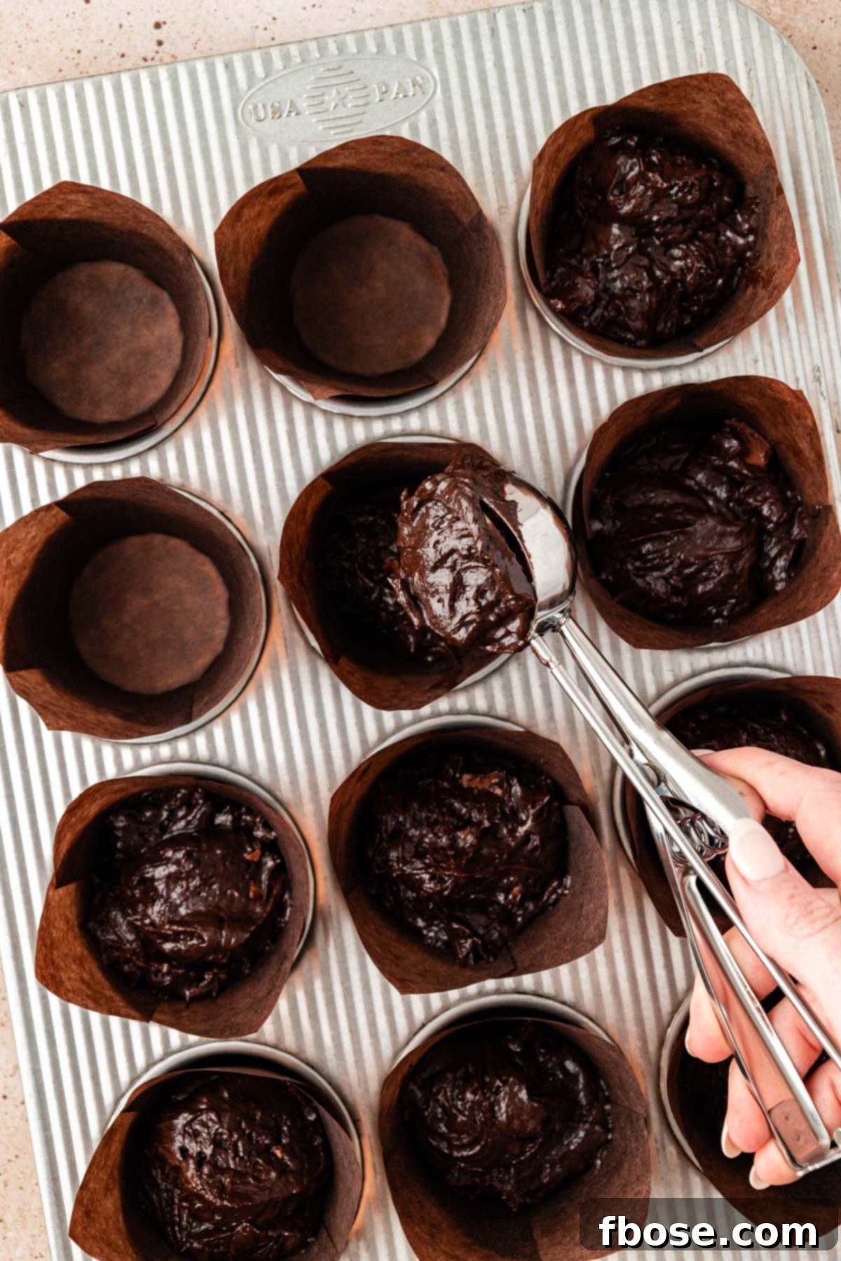 Muffin liners being expertly filled with rich chocolate muffin batter, showcasing the careful preparation before baking.