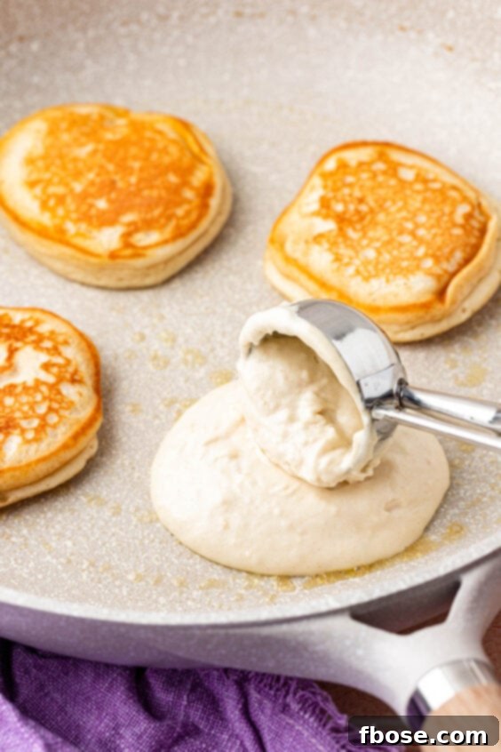 A scoop dropping pancake batter onto a hot skillet, creating individual round pancakes.