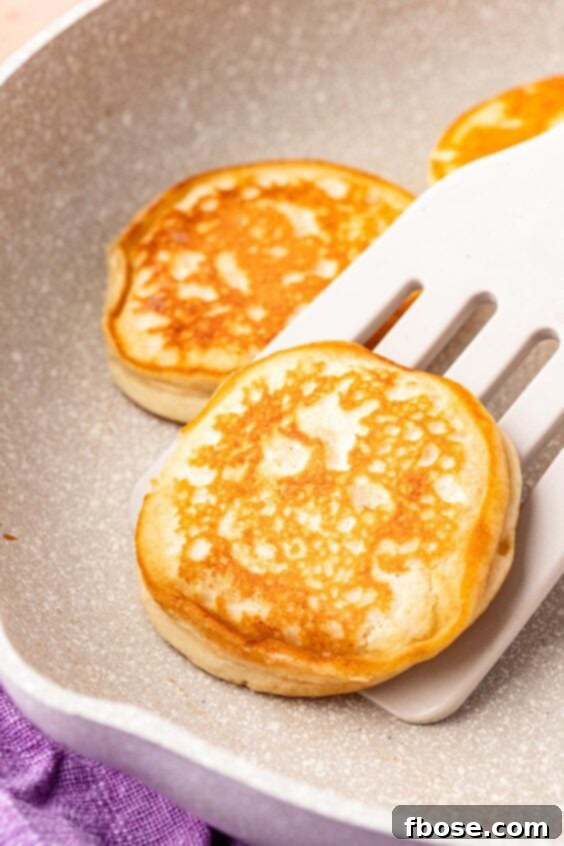 A spatula flipping a pancake in a pan, revealing a perfectly golden brown underside.