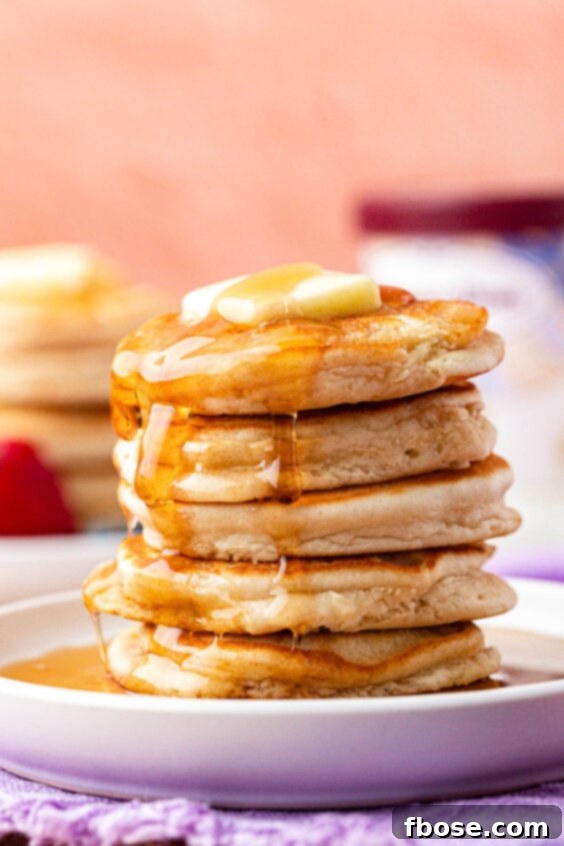 A stack of ice cream pancakes on a plate, generously covered in syrup and ready to eat.