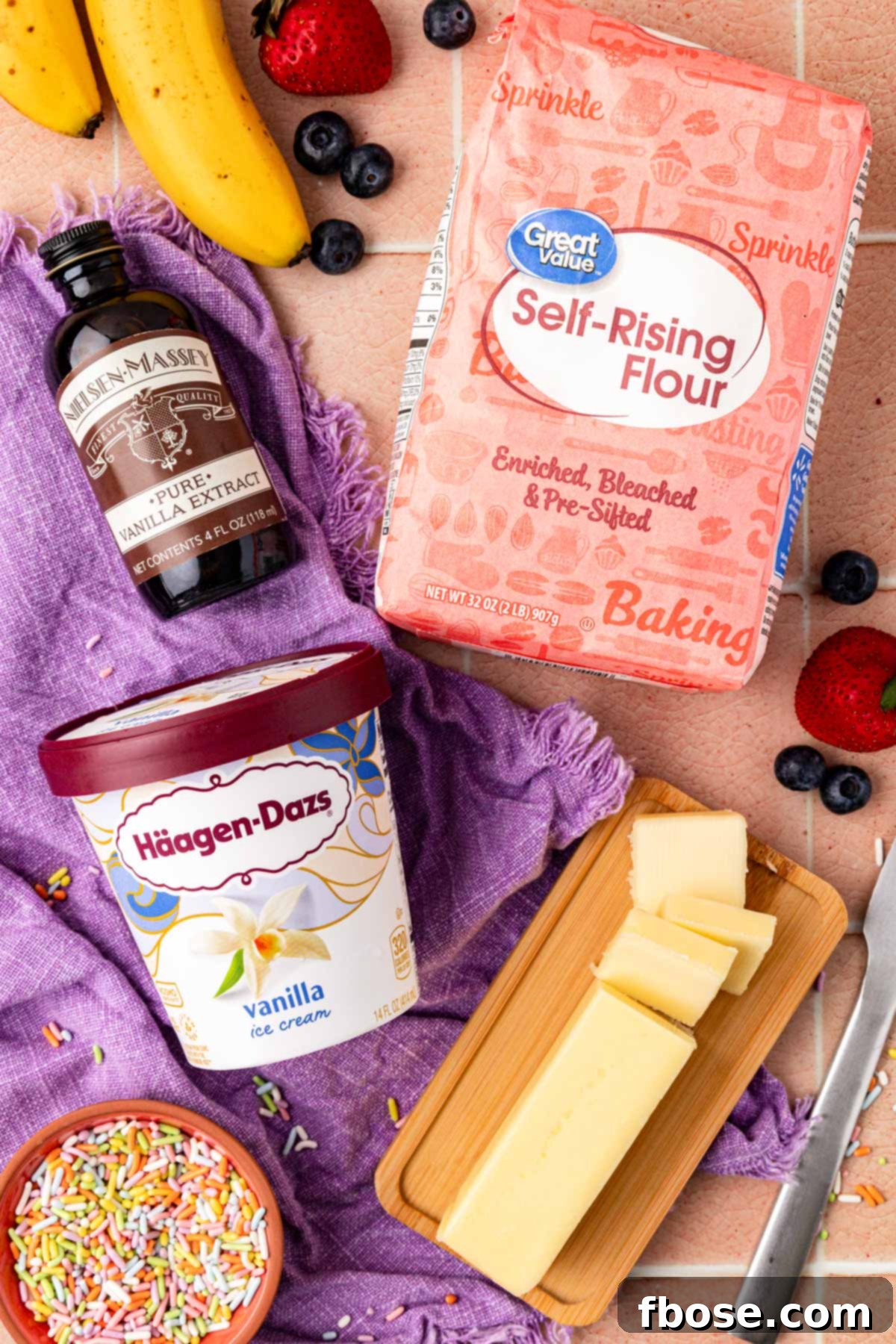 Overhead photo showing a bowl of self-rising flour, a tub of vanilla ice cream, vanilla extract, and a stick of butter, laid out as ingredients for making fluffy pancakes.