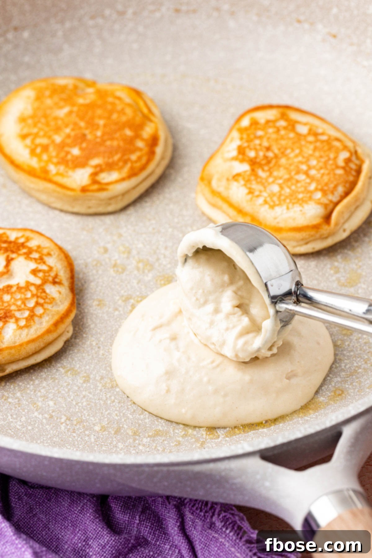 A scoop dropping pancake batter onto a hot, buttered skillet, creating perfectly round pancakes.