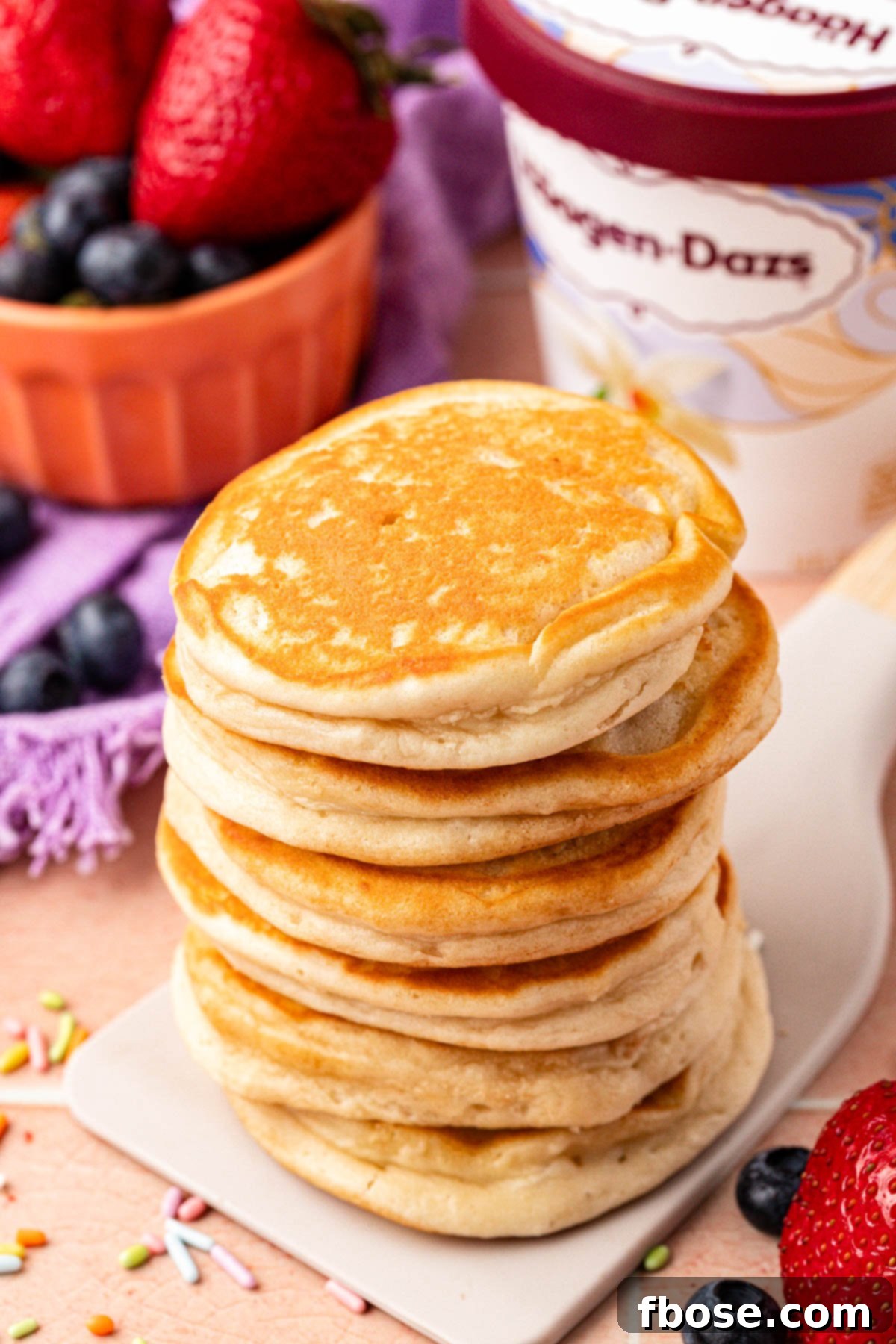 A stack of perfectly cooked, golden brown ice cream pancakes being lifted from a skillet with a spatula.