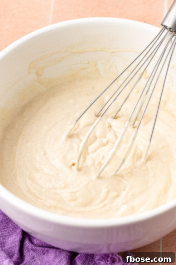 Pancake batter being whisked together in a white bowl, showing a smooth consistency with minor lumps.