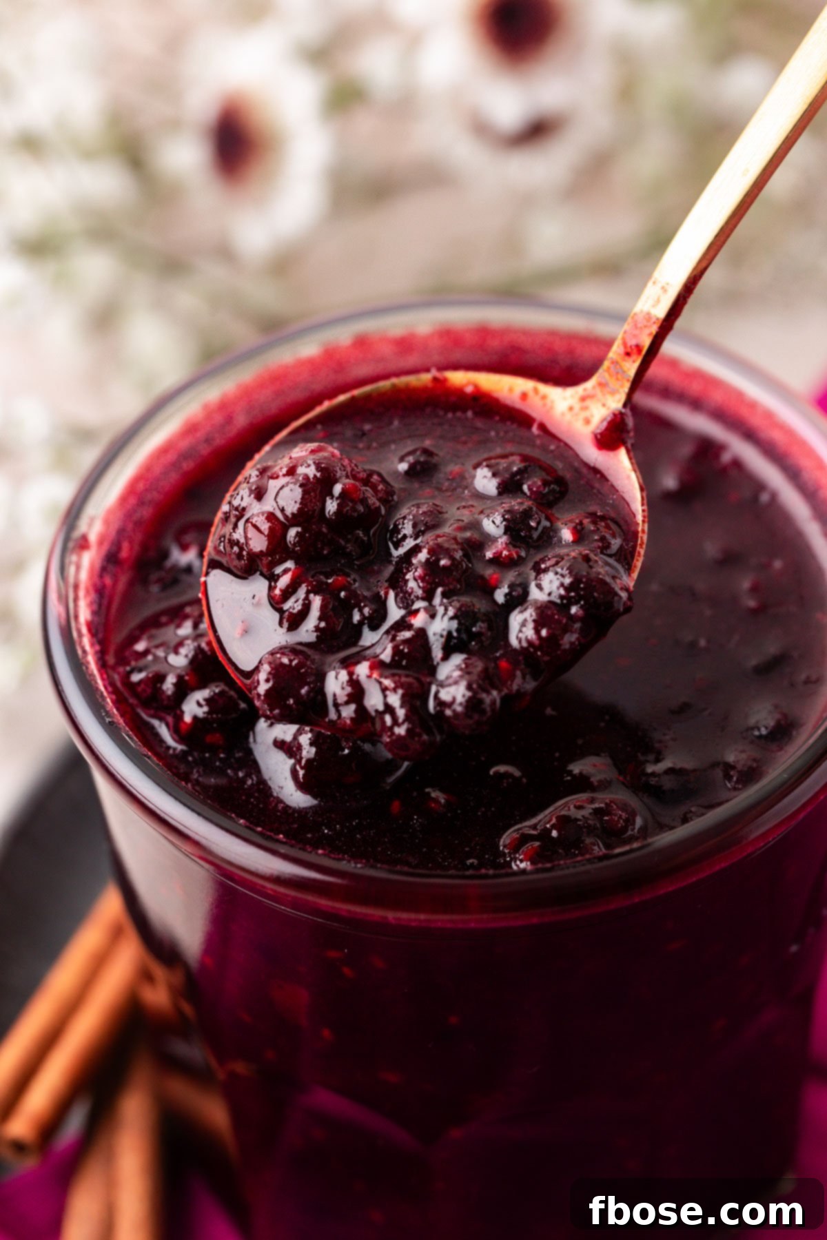 A close-up view of a jar filled with homemade berry compote, with a spoon lifting a scoop of the luscious fruit topping.