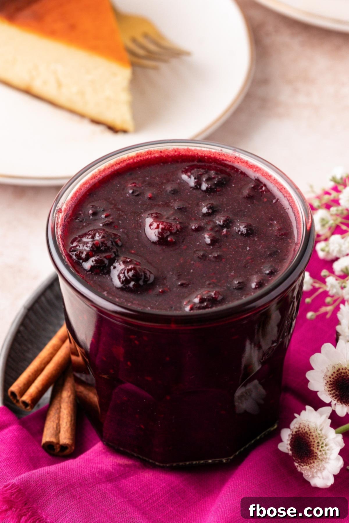 A charming jar of freshly made berry compote sits on a pink linen napkin, highlighting its inviting color and texture.