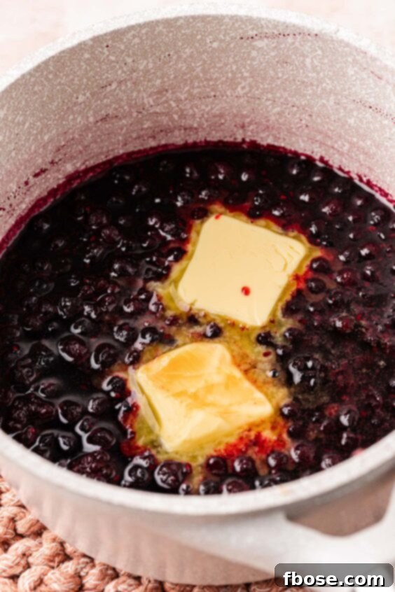 Butter being added to a pot of mixed berries that have been simmering.