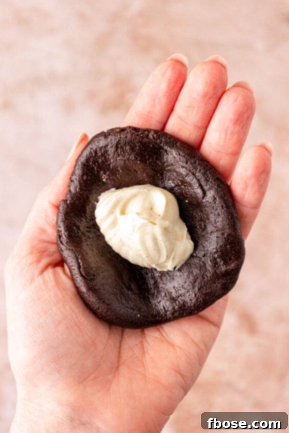 Cheesecake cookie filling in chocolate cookie dough in a woman's hand.