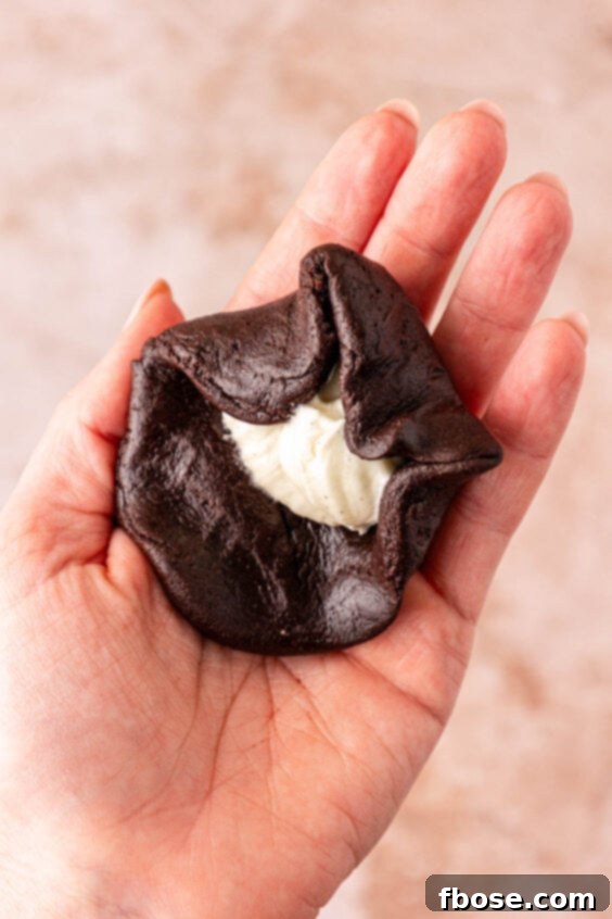 Chocolate cookie dough being wrapped around cream cheese in a woman's hand to make cookies.